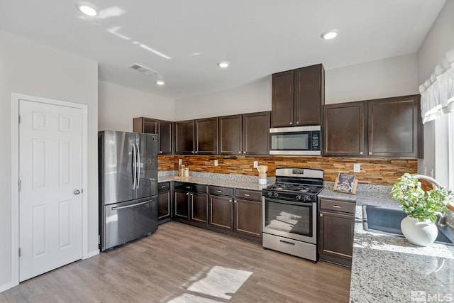 kitchen featuring light wood-style flooring, dark brown cabinetry, visible vents, appliances with stainless steel finishes, and light stone countertops