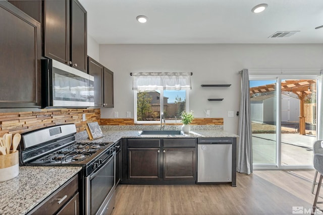 kitchen featuring visible vents, decorative backsplash, appliances with stainless steel finishes, a sink, and dark brown cabinetry