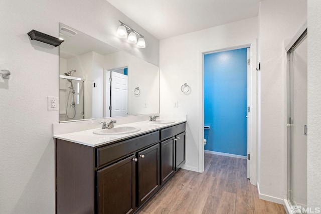 bathroom featuring toilet, wood finished floors, a sink, a shower stall, and double vanity