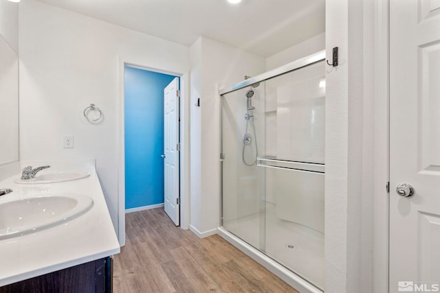 bathroom with double vanity, wood finished floors, a stall shower, and a sink