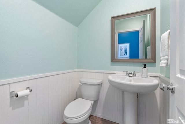 half bath with lofted ceiling, toilet, a wainscoted wall, wood finished floors, and a sink