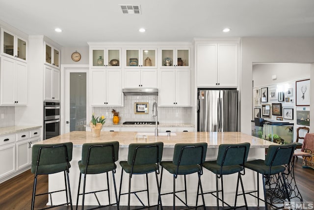 kitchen with visible vents, an island with sink, dark wood-style floors, appliances with stainless steel finishes, and white cabinetry