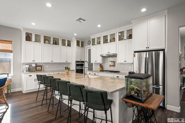 kitchen with visible vents, dark wood-style flooring, stainless steel appliances, under cabinet range hood, and a sink