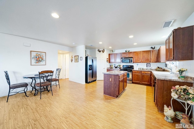 kitchen featuring stainless steel appliances, a center island, light wood-style floors, and a sink