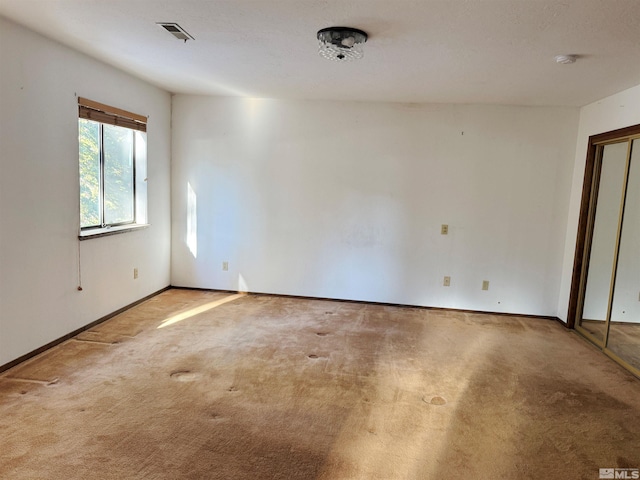 unfurnished room with carpet floors, visible vents, and baseboards