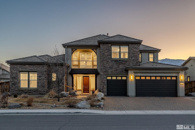 prairie-style house with stone siding, decorative driveway, a balcony, and a tiled roof