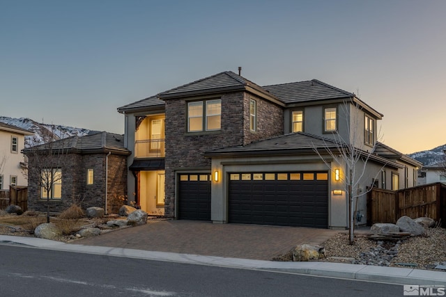 view of front of house featuring an attached garage, a balcony, fence, stone siding, and decorative driveway