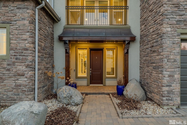 view of exterior entry with stone siding, a balcony, and stucco siding