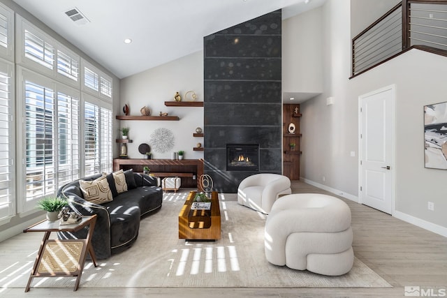 living area with a fireplace, visible vents, wood finished floors, high vaulted ceiling, and baseboards