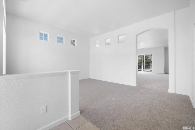 carpeted empty room with baseboards, visible vents, and arched walkways