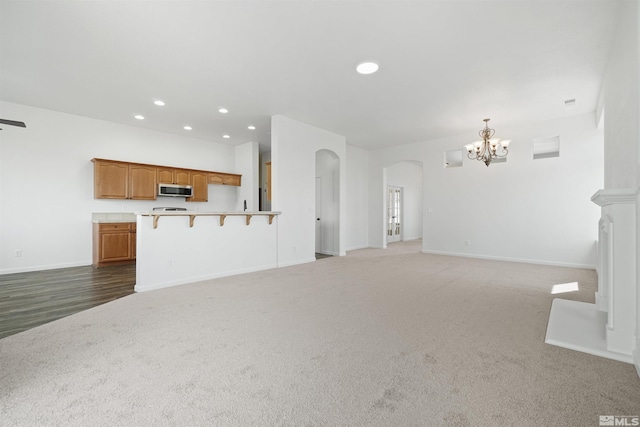 unfurnished living room with arched walkways, carpet, recessed lighting, an inviting chandelier, and baseboards