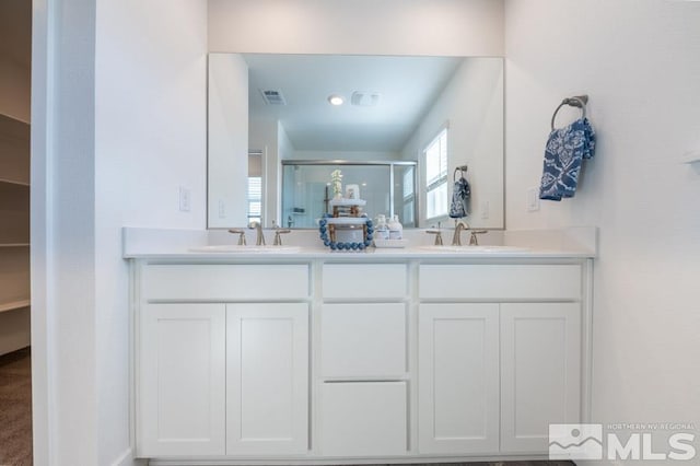 bathroom featuring double vanity, a shower stall, visible vents, and a sink