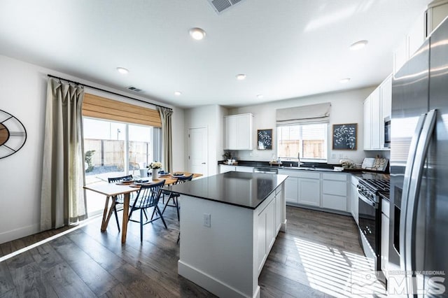 kitchen featuring dark wood-style flooring, a sink, stainless steel fridge with ice dispenser, gas range oven, and dark countertops