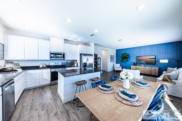 kitchen featuring dark countertops, open floor plan, a center island, stainless steel appliances, and white cabinetry