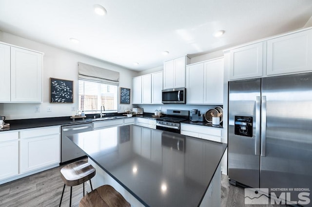 kitchen with stainless steel appliances, a breakfast bar, dark countertops, and a sink