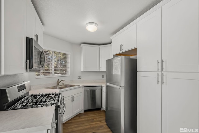 kitchen featuring dark wood finished floors, stainless steel appliances, light countertops, white cabinetry, and a sink