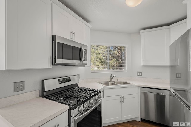 kitchen featuring stainless steel appliances, a sink, white cabinets, light countertops, and dark wood finished floors