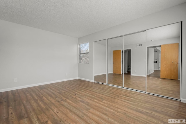 unfurnished bedroom featuring baseboards, a textured ceiling, visible vents, and wood finished floors