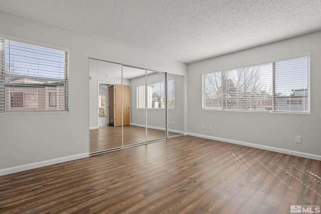 unfurnished bedroom with a textured ceiling, baseboards, and wood finished floors