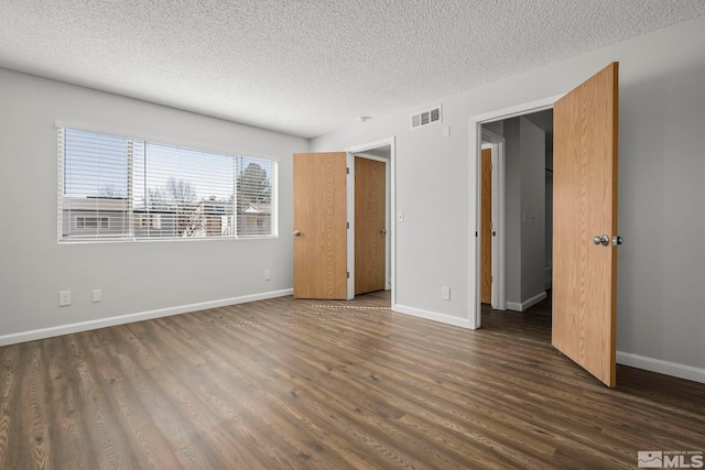 unfurnished bedroom with visible vents, a textured ceiling, baseboards, and wood finished floors