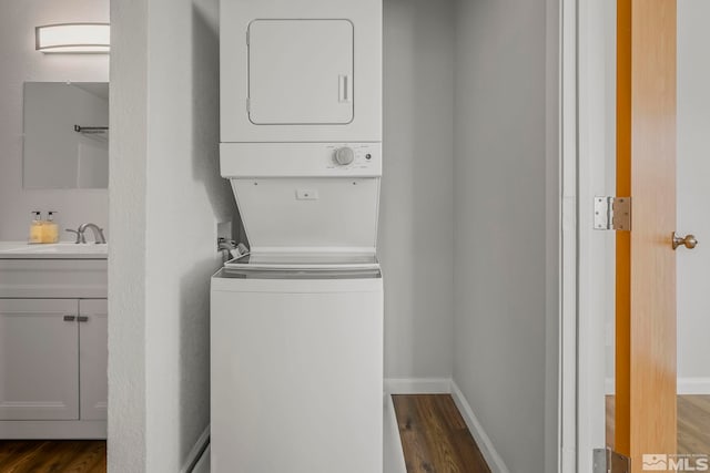 laundry room with dark wood-style floors, stacked washer and dryer, a sink, laundry area, and baseboards