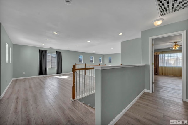 hall with baseboards, visible vents, wood finished floors, and an upstairs landing