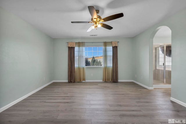 spare room with baseboards, visible vents, arched walkways, and wood finished floors