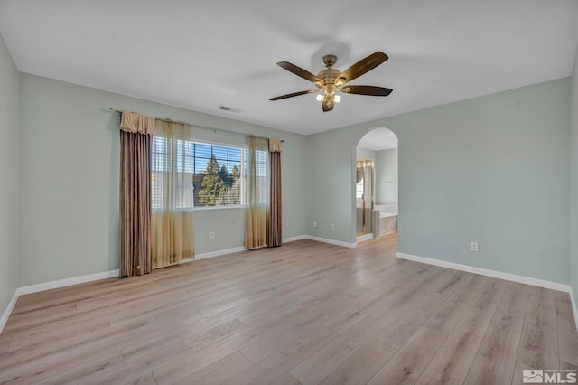 spare room featuring arched walkways, light wood-type flooring, visible vents, and baseboards