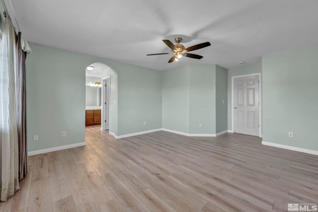 unfurnished room featuring arched walkways, ceiling fan, light wood-type flooring, and baseboards