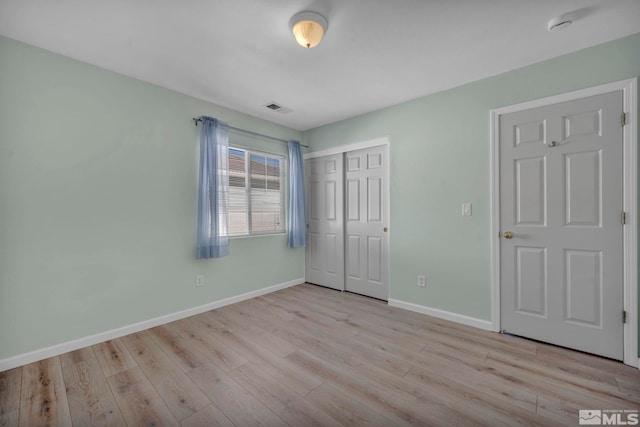 unfurnished bedroom featuring light wood-style flooring, a closet, visible vents, and baseboards