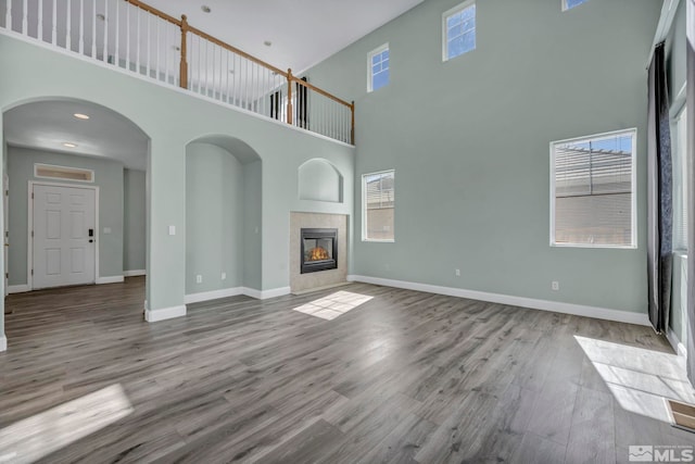 unfurnished living room featuring arched walkways, a high ceiling, wood finished floors, a tile fireplace, and baseboards