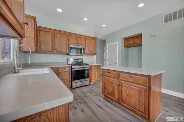 kitchen featuring brown cabinets, visible vents, appliances with stainless steel finishes, a sink, and light wood-type flooring