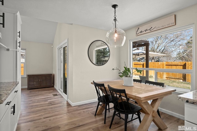 dining space featuring vaulted ceiling, light wood-type flooring, and baseboards