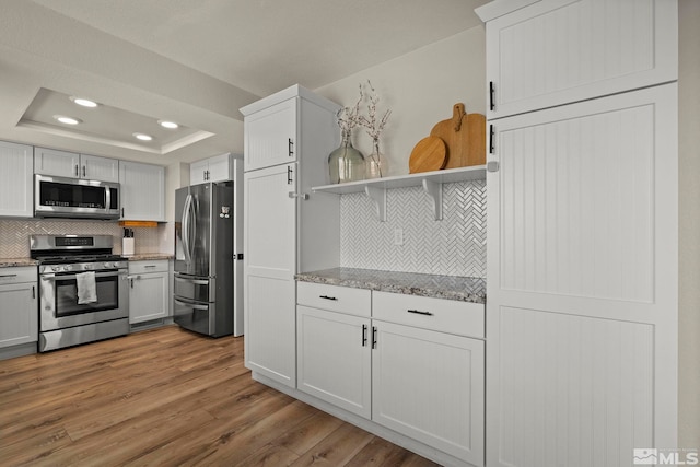 kitchen with tasteful backsplash, stainless steel appliances, wood finished floors, and a raised ceiling