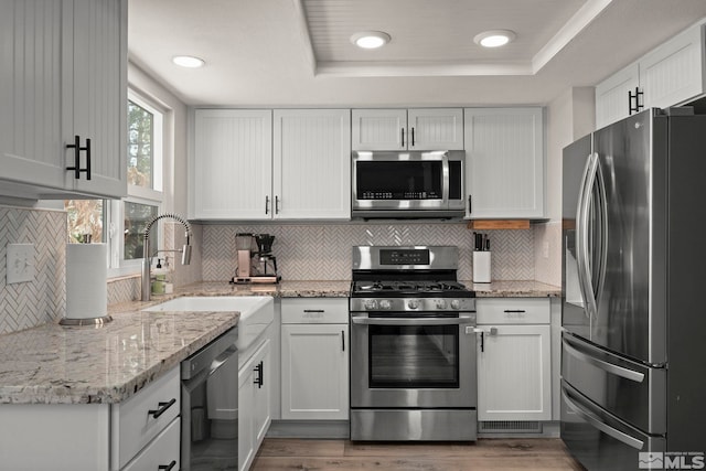 kitchen featuring stainless steel appliances, a raised ceiling, white cabinets, and light wood-style floors