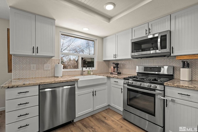 kitchen with light stone counters, decorative backsplash, appliances with stainless steel finishes, a sink, and wood finished floors