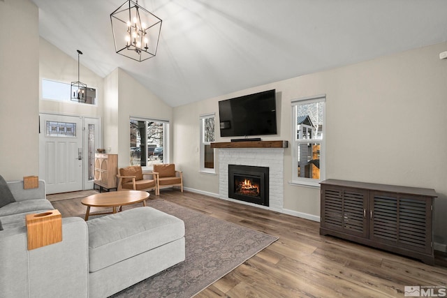 living area featuring high vaulted ceiling, a notable chandelier, wood finished floors, baseboards, and a brick fireplace