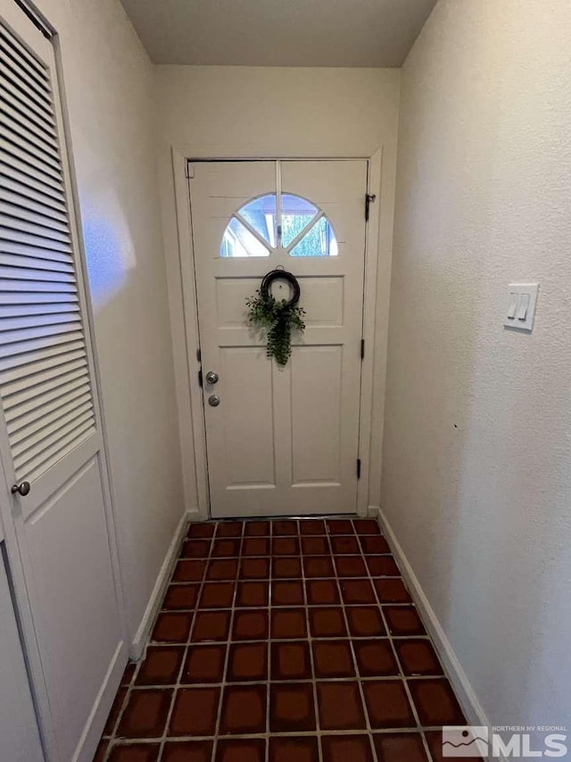 doorway featuring dark tile patterned floors and baseboards