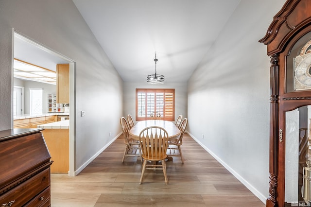 dining room featuring lofted ceiling, light wood-style floors, and baseboards