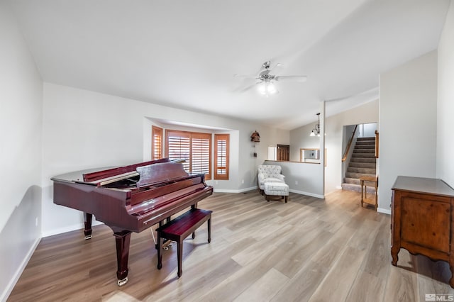 living area featuring light wood finished floors, lofted ceiling, stairway, a ceiling fan, and baseboards