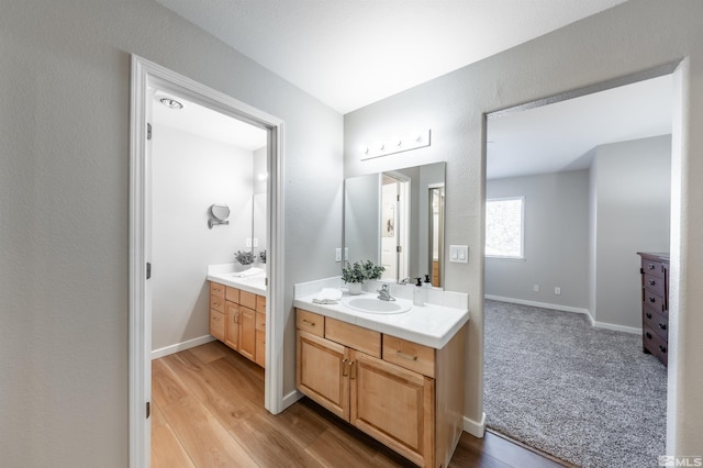 bathroom featuring wood finished floors, two vanities, a sink, and baseboards