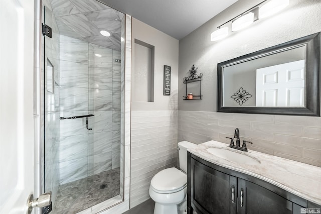 bathroom with vanity, a shower stall, toilet, and tile walls