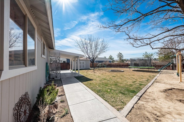 view of yard with an outbuilding, a playground, a fenced backyard, a storage unit, and a trampoline