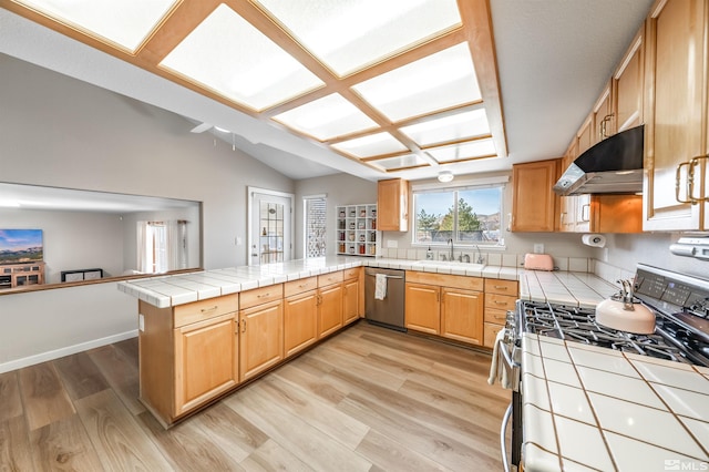 kitchen featuring tile counters, a peninsula, stainless steel appliances, under cabinet range hood, and a sink