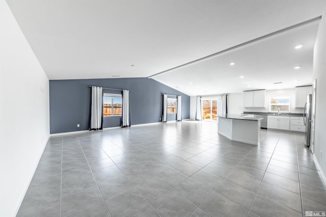 unfurnished living room featuring lofted ceiling, light tile patterned floors, recessed lighting, a sink, and baseboards