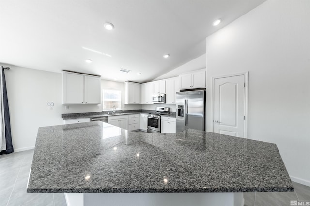 kitchen with stainless steel appliances, a spacious island, white cabinets, a sink, and dark stone countertops