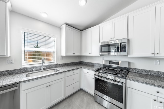 kitchen featuring light tile patterned floors, appliances with stainless steel finishes, stone counters, white cabinetry, and a sink