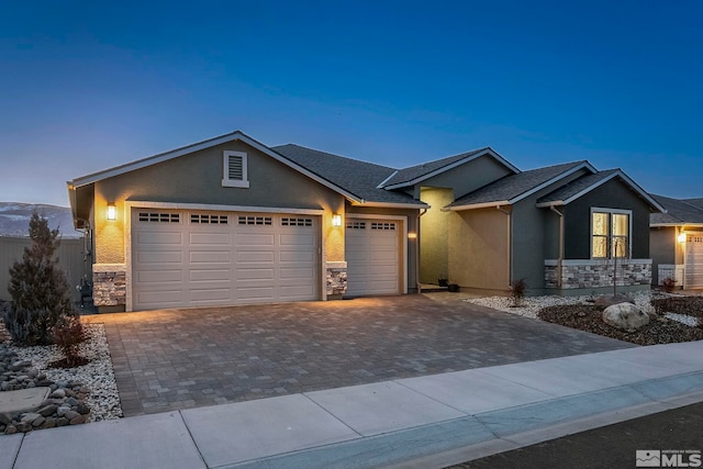 view of front of house featuring a garage, stone siding, decorative driveway, and stucco siding