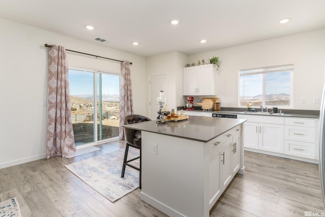 kitchen with light wood-style flooring, a sink, white cabinets, a center island, and a kitchen bar