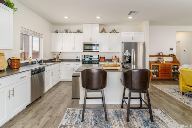 kitchen with stainless steel appliances, a sink, visible vents, light wood finished floors, and a kitchen bar